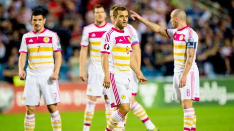 SNS Scotland players wearing white shirts with yellow and pink hoops, white shorts and matching socks.