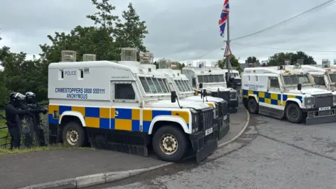 PA Media A row of PSNI vans parked on the side of a road. 
