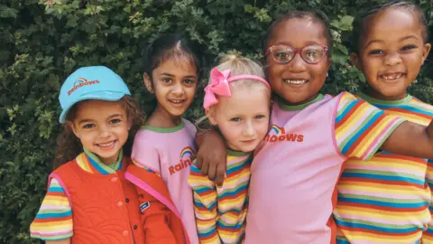 Emily Stein/Girlguiding Five young girls wearing new caps, t-shirts and gilets with rainbow designs as part of the new Rainbows uniform range.