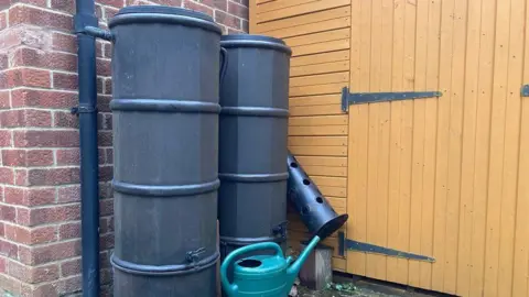 Two water butts next to house and guttering with a watering can