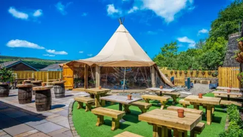 A photo of the outdoor space, including a large tipi, outdoor benches, pergola and patio at the Eagle and Child pub in Ramsbottom.