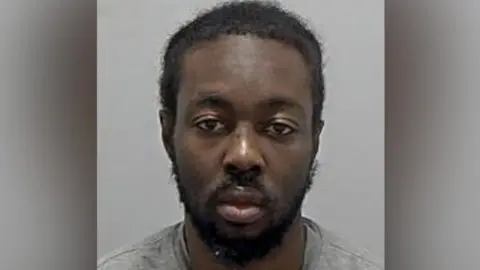 Bedfordshire Police Tyreese Kamau: A man with black hair and a black beard wearing a grey and round necked t-shirt in his custody photo