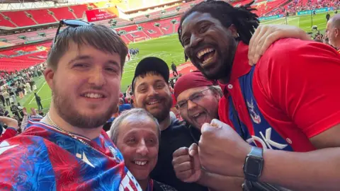 Dan Turner Browne Five people take a close-up selfie inside a football stadium, wearing Crystal Palace shirts.