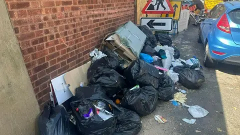 Black bin bags and overflowing rubbish on the pavement.
