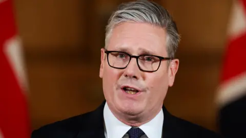 PA Media Sir Keir Starmer dando uma declaração com dois Jacks Union em segundo plano.