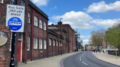 A sign to the left-hand side of the picture, in front of a row of buildings. The sign says bus gate 180 yards ahead.