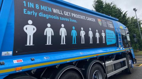 The blue bin lorry has a design showing the silhouettes of eight men, seven of them coloured white and one blue