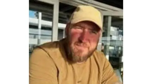 James has a light brown beard and wears a yellow cap and t-shirt.