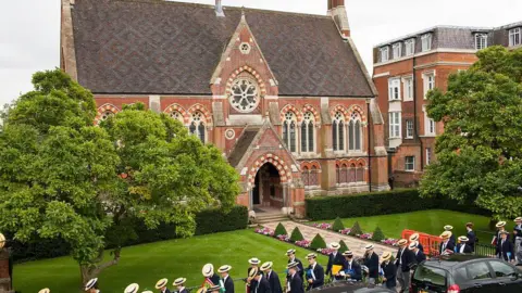 Getty Images Outside of school - a brick building. School boys walk past wearing boater hats. 