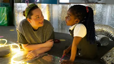 BID Leicester A woman with antennae headband interacts with a young girl in a classroom setting 