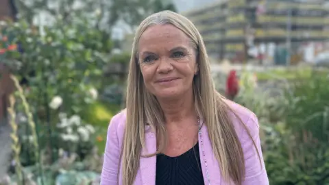 Gaynor Hutton wearing a pink blazer smiling for a photograph in an outside garden