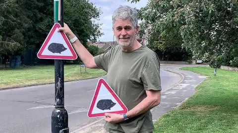 Christian Vassie Christian Vassie, Liberal Democrat ward councillor for Wheldrake, with hedgehog warning signs at the side of a curved road.
