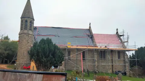 Hudswell Community Charity A Victorian village church surrounded by scaffolding with tarpaulin over the roof. 