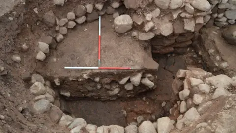 Stones in the ground are arranged in a circle. A red pole has been placed in the middle.