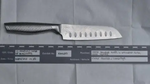 Cambridgeshire Police A police image of a large-bladed chopping knife placed on paper, with labels under it that read the date/time it was found, the exhibit number and where it was found.