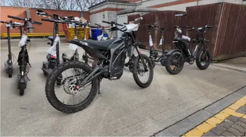An electric motorbike, electric bike and e-scooters that were seized by the police are parked up in the car park of a police station in Kent.