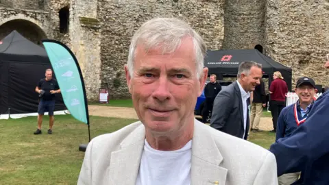 Matt Marvel/BBC Derek Davis, who is the economic development portfolio holder for Babergh District Council. He is wearing a cream blazer over a white T-shirt. He is looking into the camera.