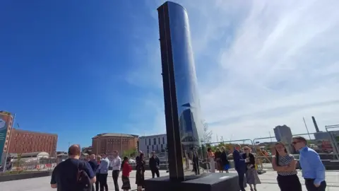 A none metre high sculpture. People are standing around it. Construction work is going on in the background. 