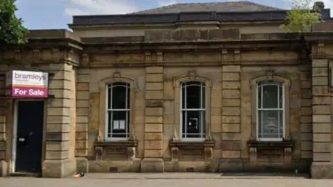 Google A stone court building with white windows and a for sale sign