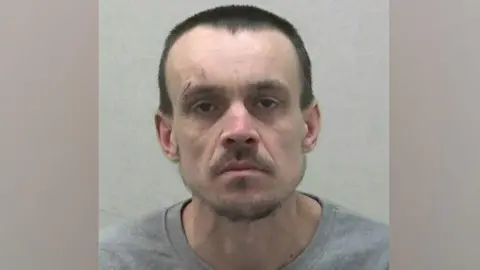 Northumbria Police Mugshot of Craig Howse who is wearing a grey sweatshirt. He has very short dark hair and slight beard and moustache and has a cut above his right eye. 