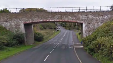 A stone bridge over a road with is stretching downhill into the distance.