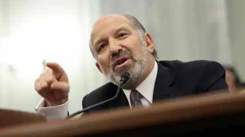 Howard Lutnick speaks into a microphone at this Senate confirmation hearing. He is pointing his finger as he speaks. 