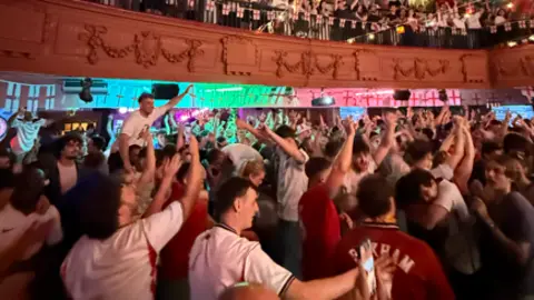 The Grosvenor England fans, in red and white shirts, celebrate with their arms in the air in Manchester