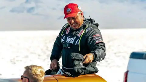 Speed Demon 715 Chris Raschke wearing a read hat and a race suit