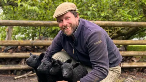 Farmer Tom Martin cuddles four black lambs