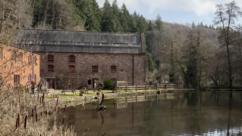 A photo of Soudley Ponds in the Forest of Dean. It shows a building surrounded by trees next to a pond