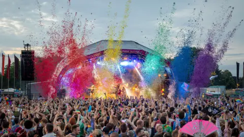 Dan Weill A large crowd watching an outdoor performance at Bristol Pride 2025. They are all stood facing the stage and there is rainbow confetti above the crowd.