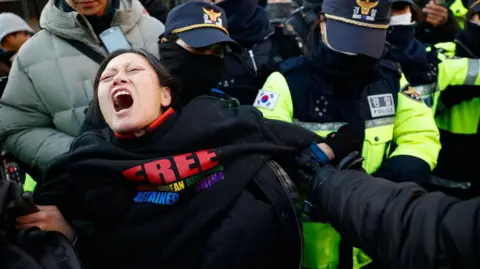 Getty Images Petugas polisi mengeluarkan pendukung Presiden Korea Selatan yang dimakzulkan Yoon Suk Yeol dari luar kediaman resminya di Seoul, Korea Selatan, pada 2 Januari 2025.