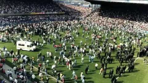 An ambulance and football fans and police officers on the pitch during the Hillsborough stadium disaster.