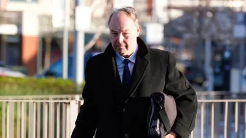 PA Media A white brown hair man walking wearing a suit and a long dark coat 