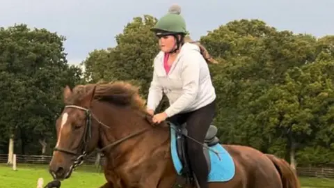 Lee Maisy on a brown and white horse riding in a field and wearing a green and grey helmet.