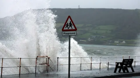 Reuters A high wave crashes against a sea wall with a tall 'playground' sign in front of it in Carnlough, Northern Ireland 