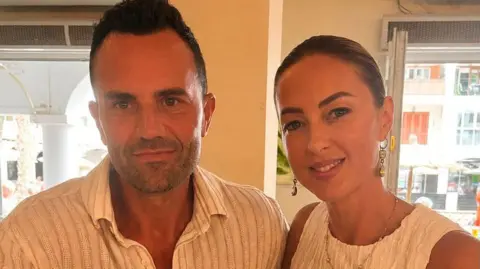 Ainsley Lawless A man and a woman both wearing white, smiling at the camera.