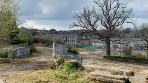 Mayday Saxonvale Derelict Saxonvale site with bare tree, and fences. Buildings and homes are in the background.
