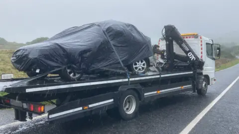 Car covered with black tarpaulin, on a moving truck