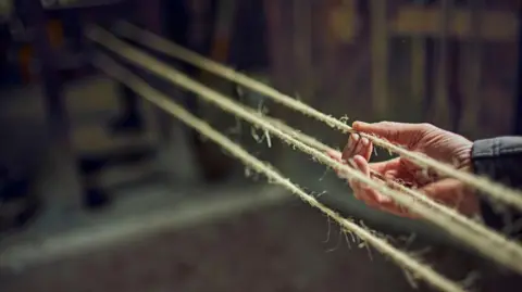 Getty Images A traditional rope walk, with thin fibres stretched taunt across a gap. A hand can be seen holding one of the fibres.
