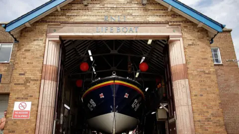 A blue, yellow and red lifeboat in a brick shed boat house in Scarborough.