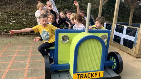 Around 15 children are playing on their new wooden tractor with the registration number Tracky 1 