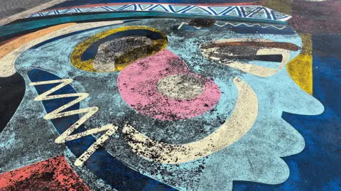 A section of the mural showing a profile of a face. The paint has faded and there are patches of black showing through.