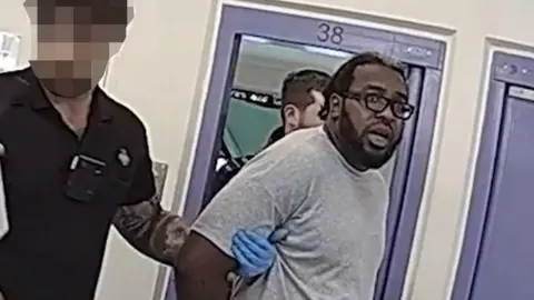 Nottinghamshire Police An image of a man wearing glasses with his arms behind his back, being detained by a prison officer