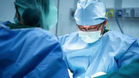 Getty Images Two surgeons, dressed in surgical scrubs, performing an operation