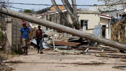 Orlando Barria/EPA/Shutterstock People walk down a street littered with debris after Hurricane Melissa in Falmouth, Jamaica.