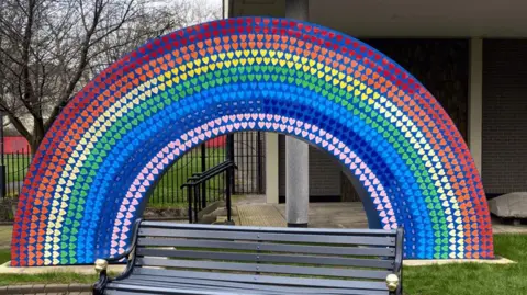 Doncaster and Bassetlaw Teaching Hospitals NHS Trust A large memorial in the shape of a rainbow covered in colourful hearts, a bench in the foreground