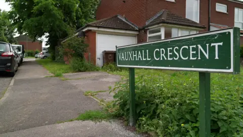 Road sign of Vauxhall Crescent with cars parked on the right hand side of the road. Houses can be seen on the left hand side of the photo with a pavement alongside it