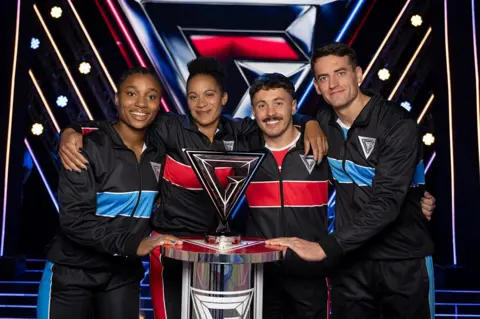 BBC/Hungry Bear Four Gladiator contenders stand around the winners trophy while smiling at the camera