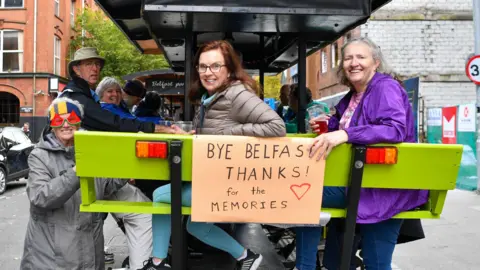 Pacemaker Passengers of the cruise vessel  smiling connected  a brew  motorcycle  successful  Belfast with a motion   that says 'Bye Belfast, acknowledgment  for the memories'